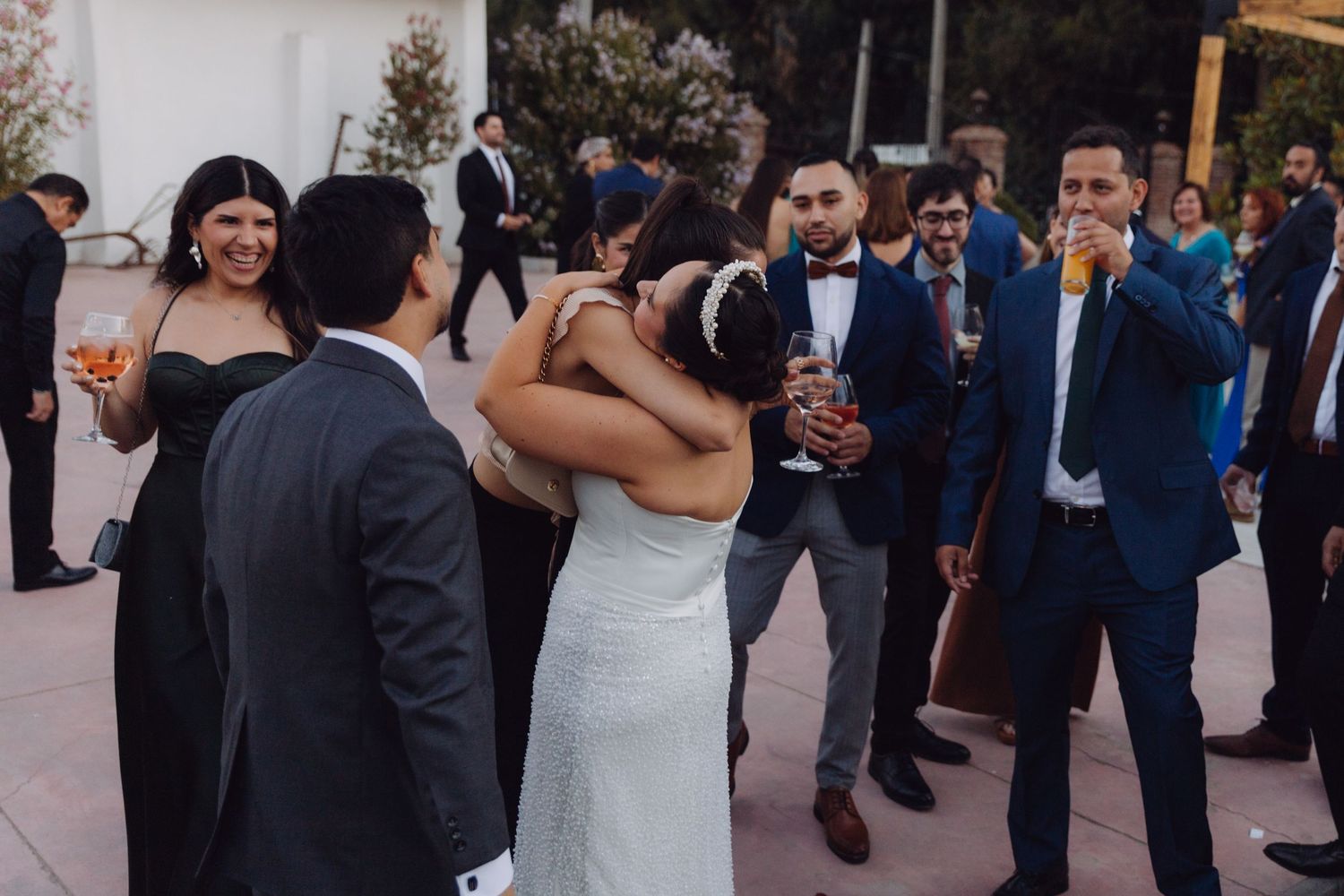 Bride shares a heartfelt hug with a guest while others celebrate at an outdoor wedding reception.