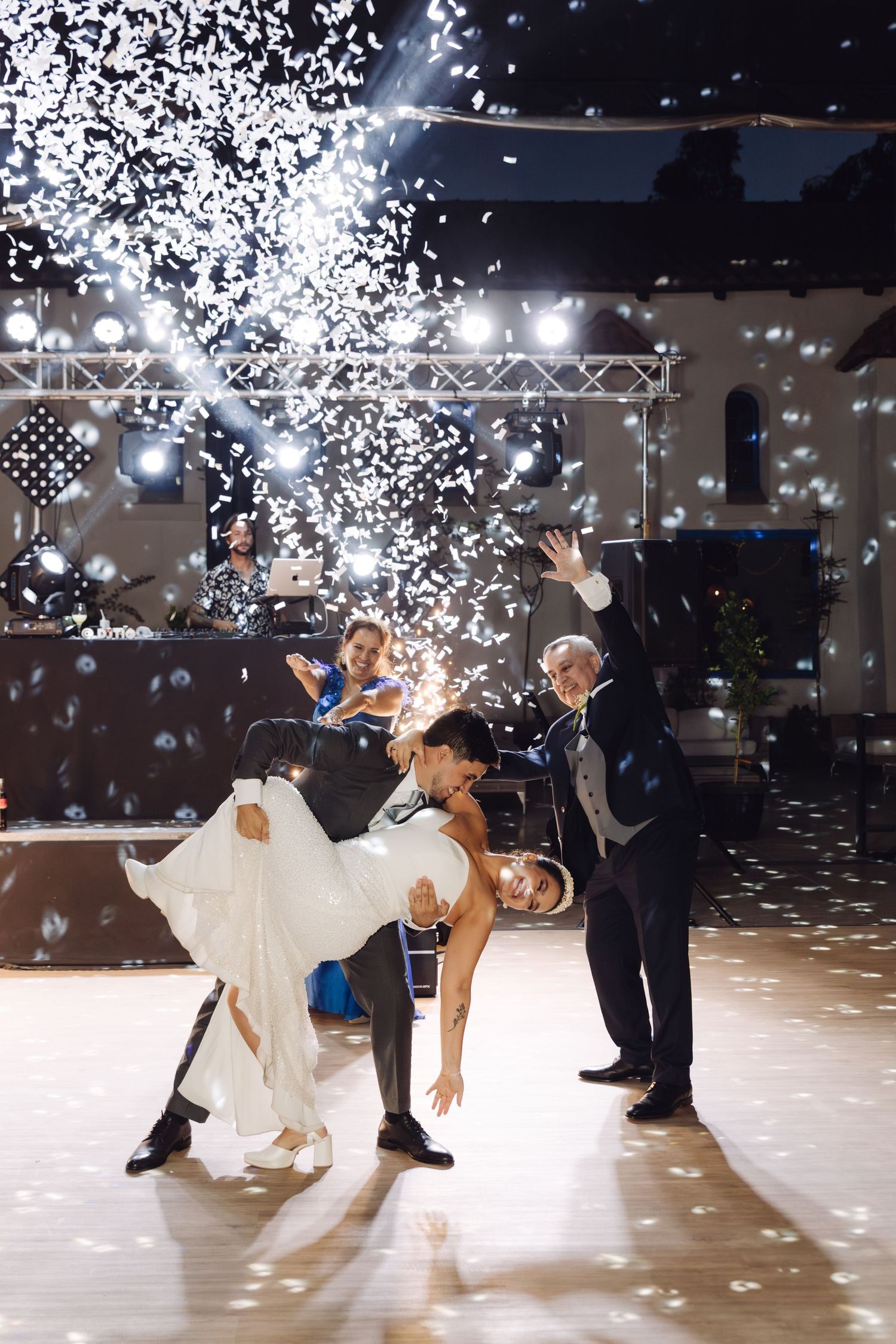 Bride and groom share a romantic dip dance move surrounded by white confetti at their wedding reception.