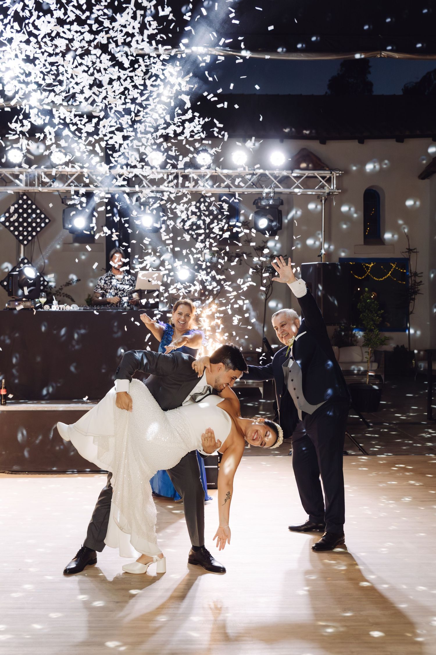 Groom dips bride dramatically on the dance floor as confetti falls during their first wedding dance.