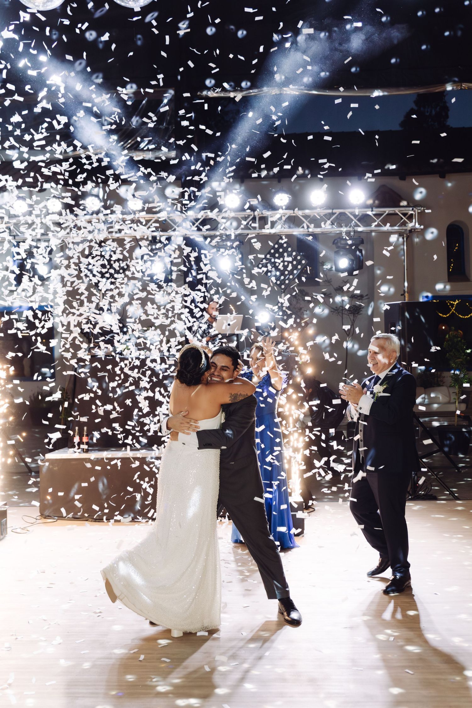 Bride and groom share their first dance embracing as white confetti fills the air at their reception.