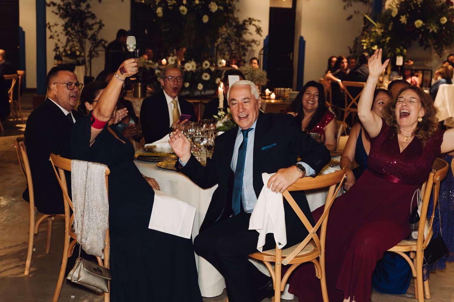 Excited wedding guests celebrate and cheer at their table during the wedding reception dinner.