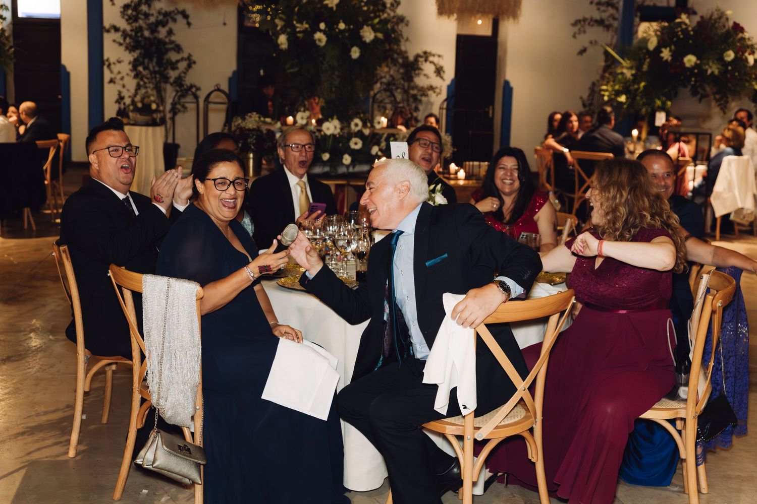 Wedding guests toast and laugh joyfully together at their decorated reception dinner table.
