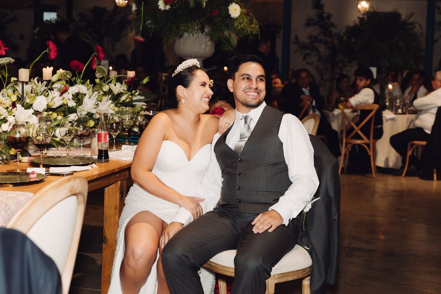 Smiling bride and groom sit together at their sweetheart table during their wedding reception.