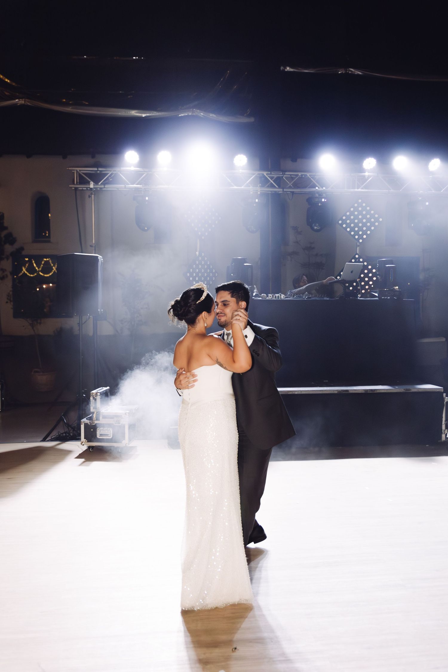 Bride and groom share their first dance in a romantic fog-filled venue illuminated by dramatic stage lighting.