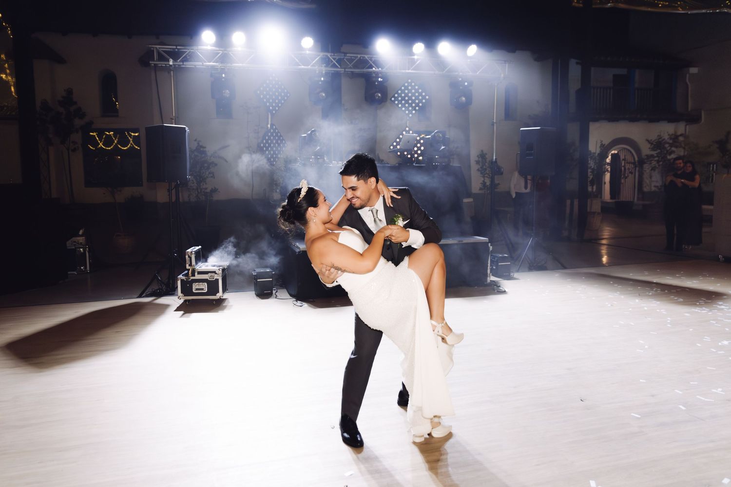 Groom dips bride dramatically on the wedding dance floor surrounded by atmospheric fog and bright stage lights.