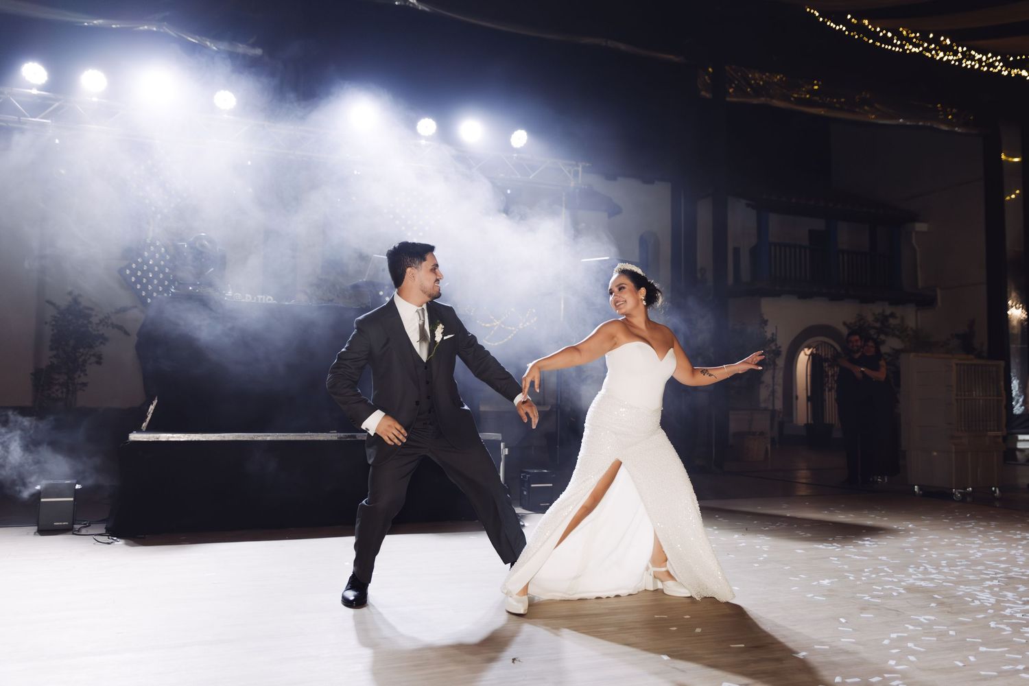 Bride and groom perform an elegant choreographed first dance on a foggy dance floor with bright venue lighting.