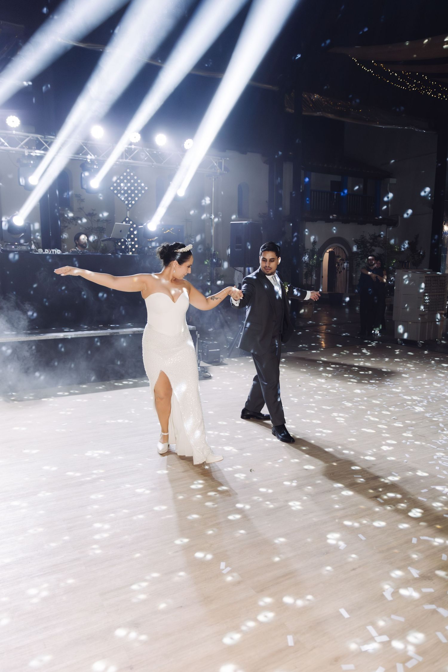 Bride and groom dance gracefully as white confetti falls around them under dramatic blue stage lighting.