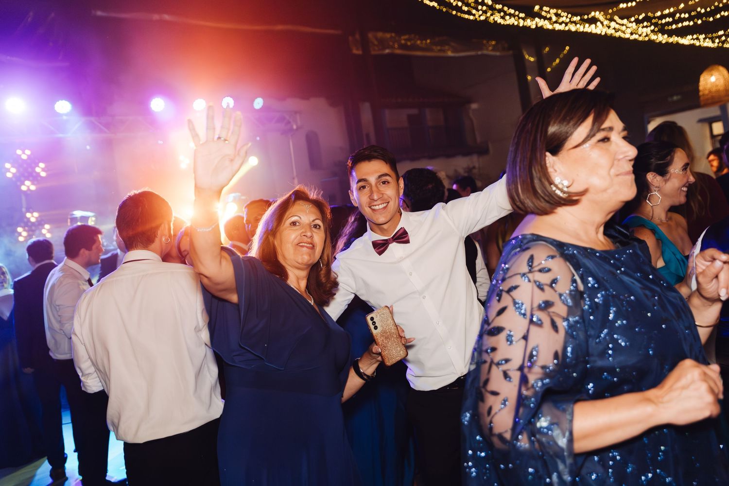 Wedding guests celebrate and dance joyfully under colorful lights during a lively wedding reception party.