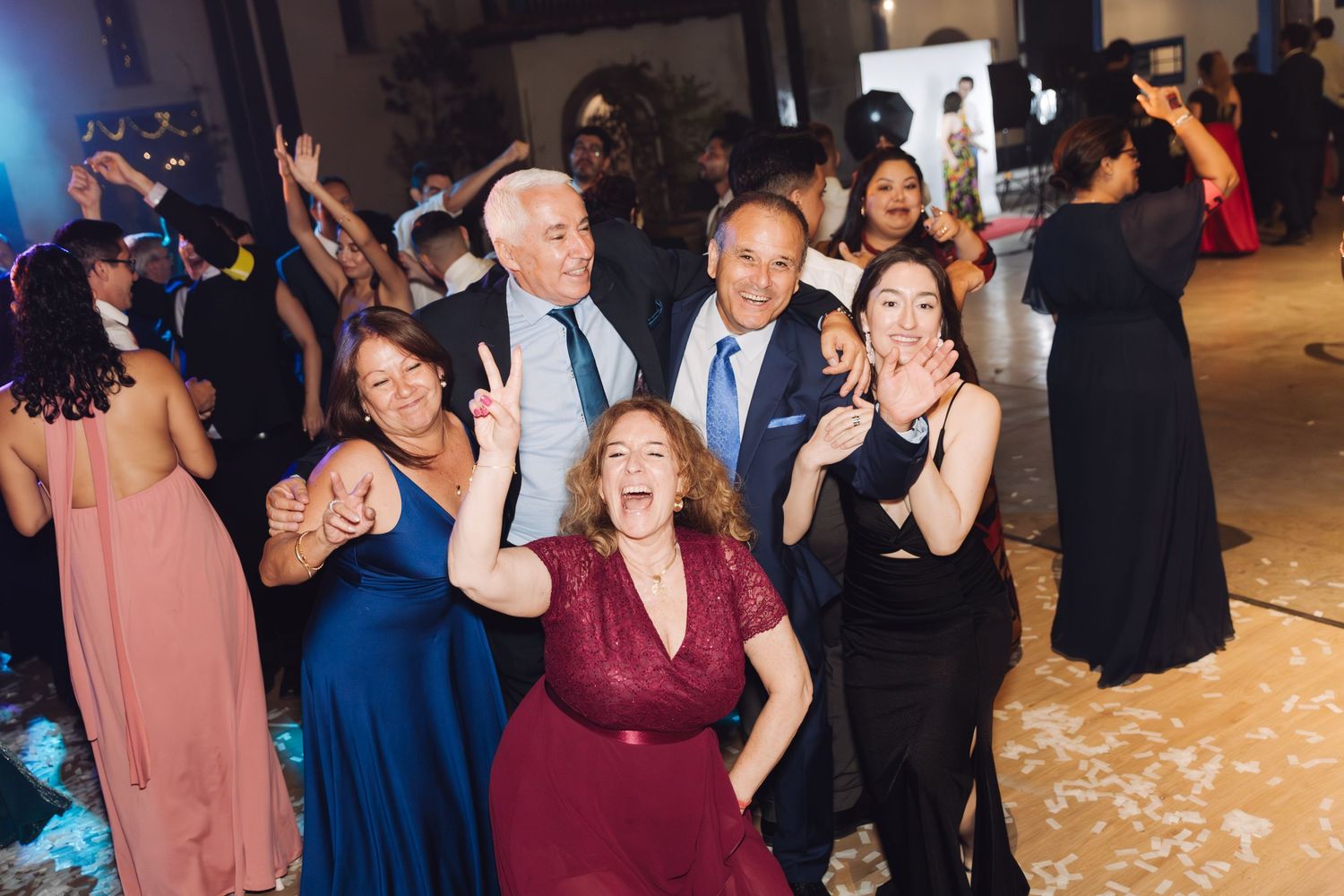 Group of happy wedding guests pose and smile together on the dance floor during a festive wedding reception.