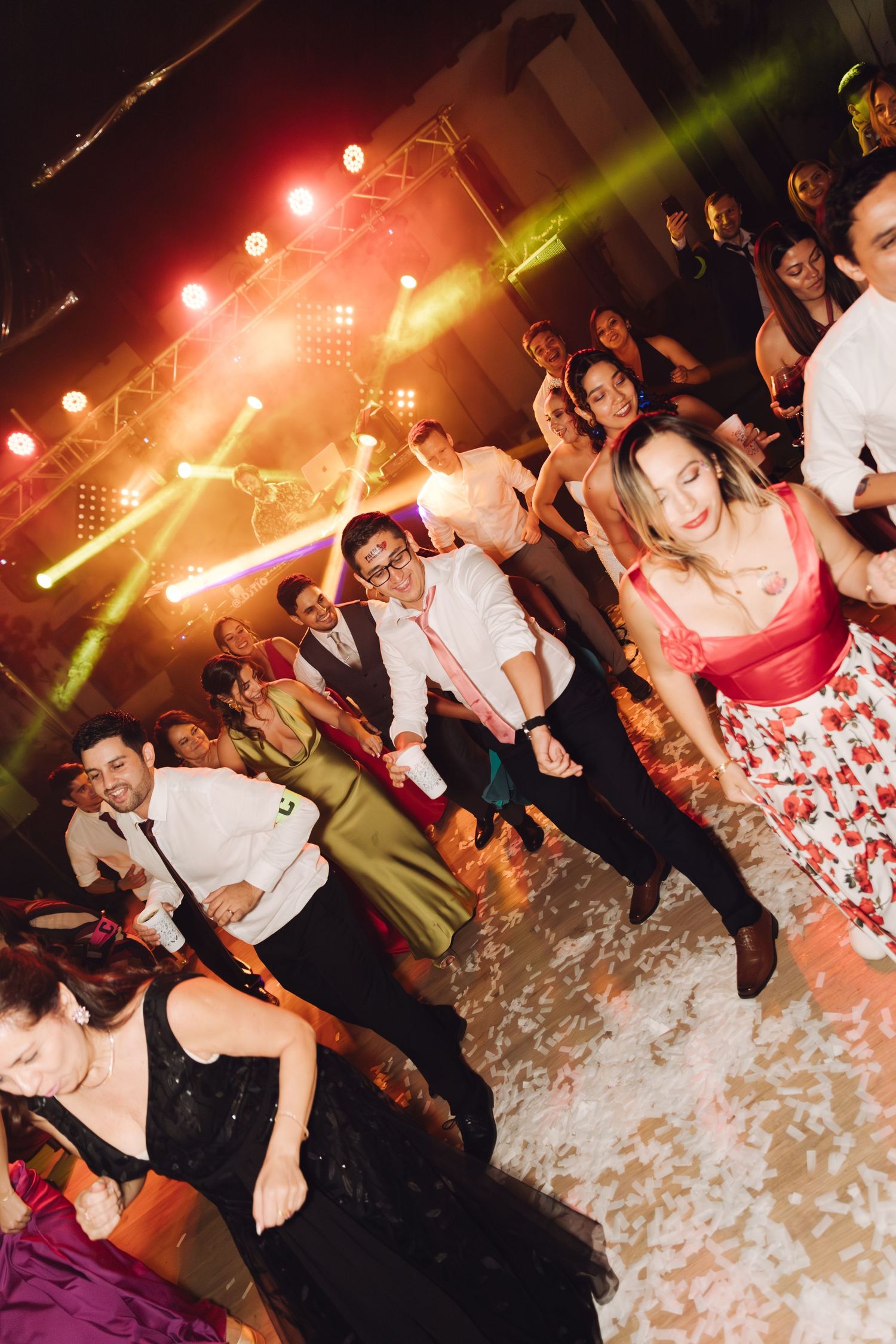 Wedding guests dancing energetically under colorful stage lights at a lively evening reception.