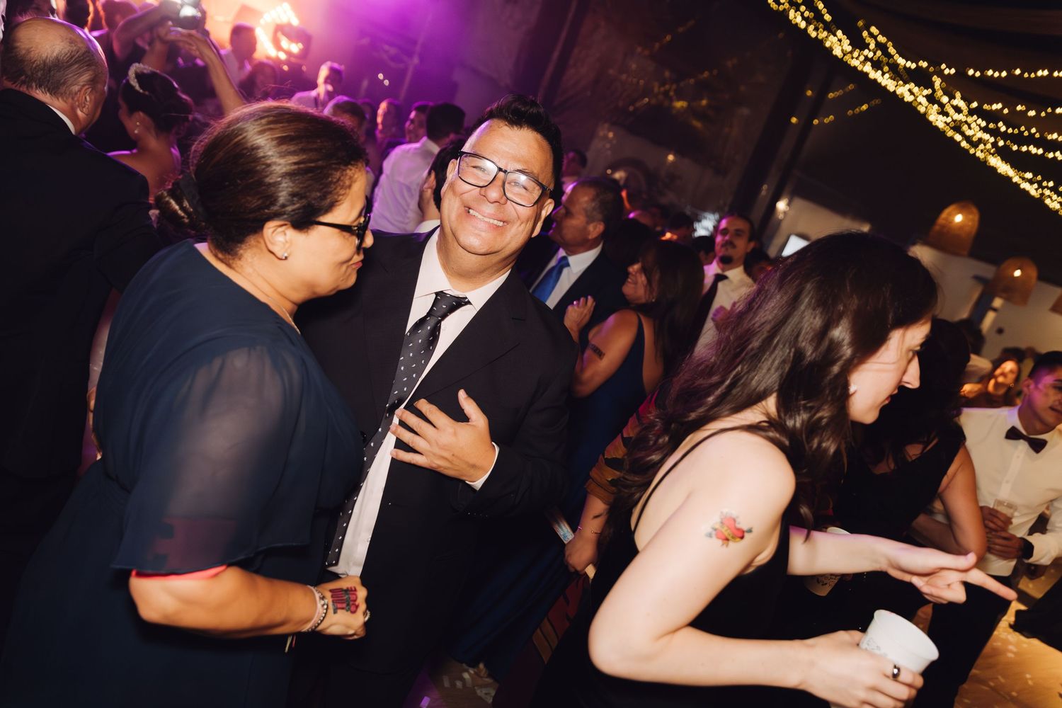 Wedding guests smiling and socializing on the dance floor at an evening reception.