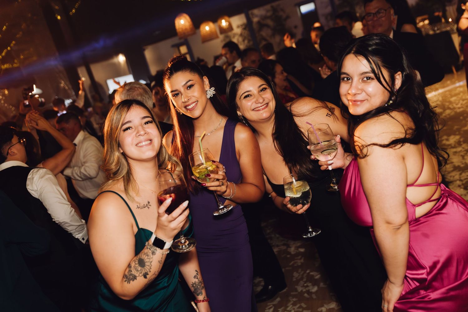 Four elegantly dressed women posing together with drinks at a wedding reception.