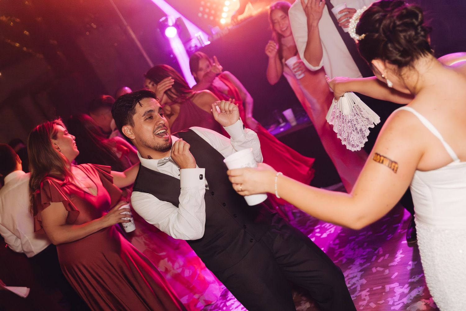 Bride and groom dancing energetically with guests at a lively wedding reception party.