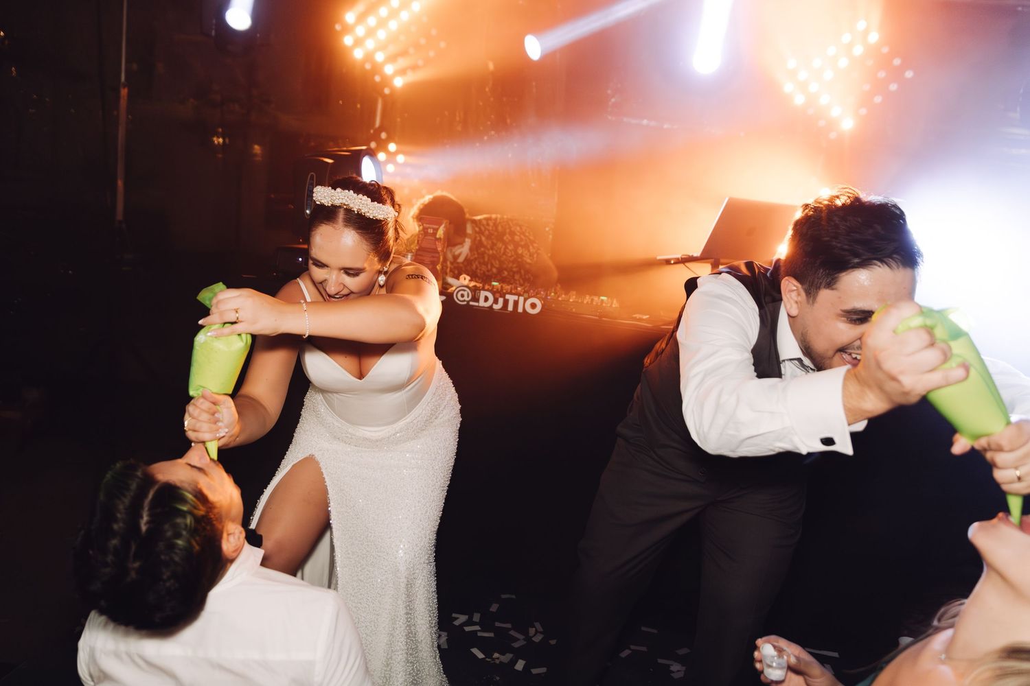 Bride and groom sharing a fun moment with green bottles on the wedding dance floor.
