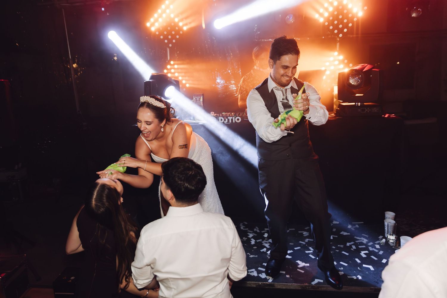 Bride and groom sharing a playful moment with guests on a dramatic lit stage.