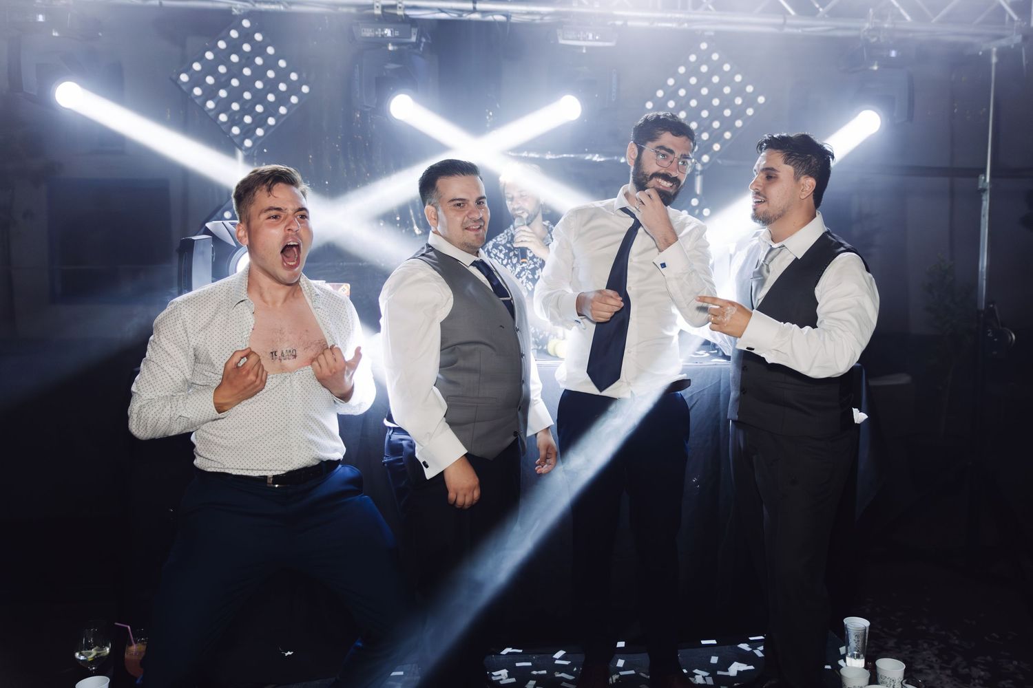 Four men singing and performing together on a smoky stage at a wedding reception.