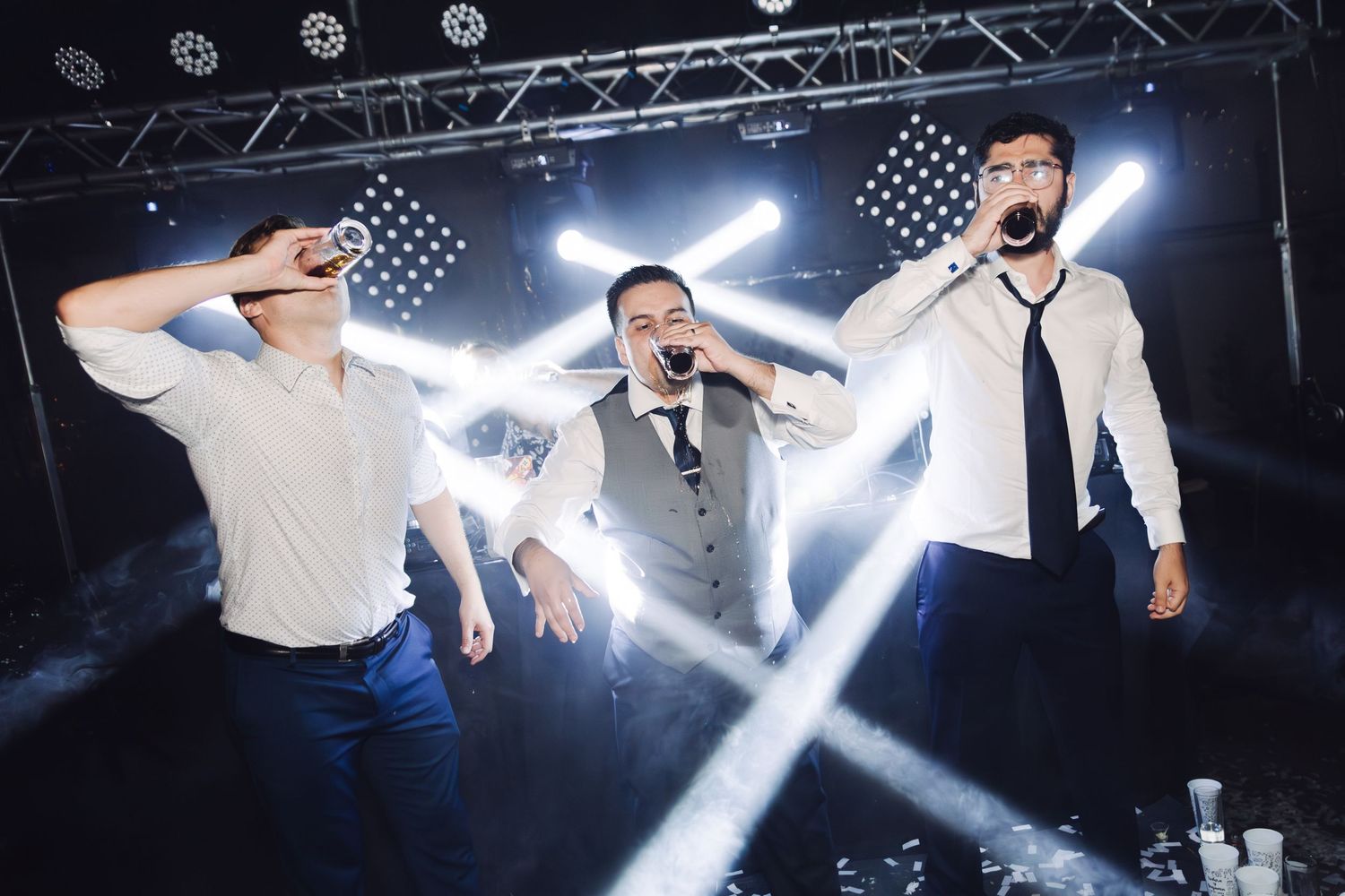 Three men performing and singing together under bright stage lights at a wedding.