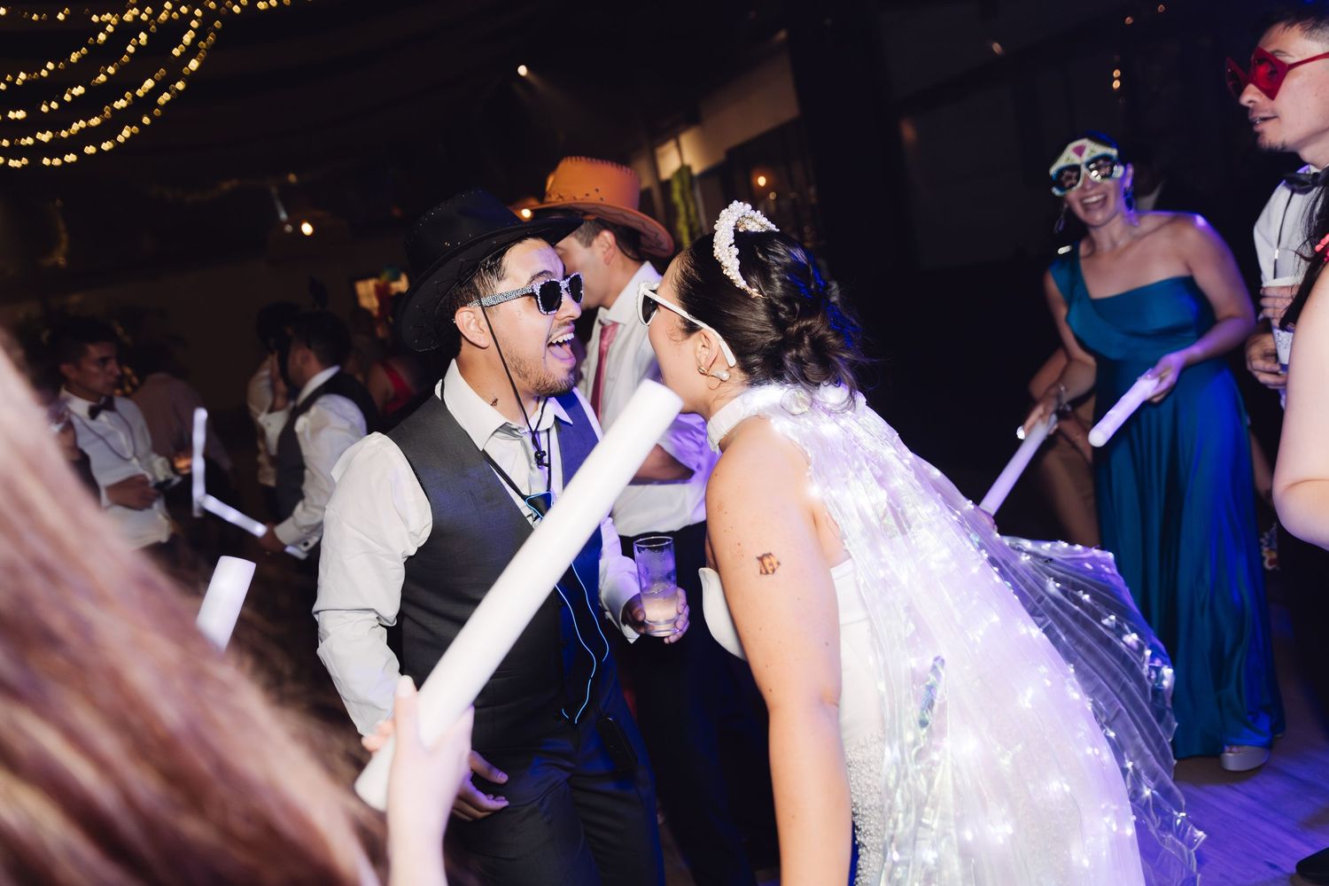 Bride and groom dancing at wedding reception wearing masks and holding glow sticks.