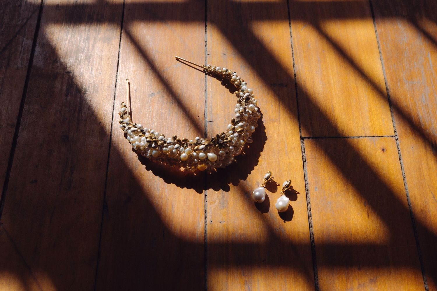 Gold crescent moon bridal crown with pearl earrings on wooden floor in sunlight.