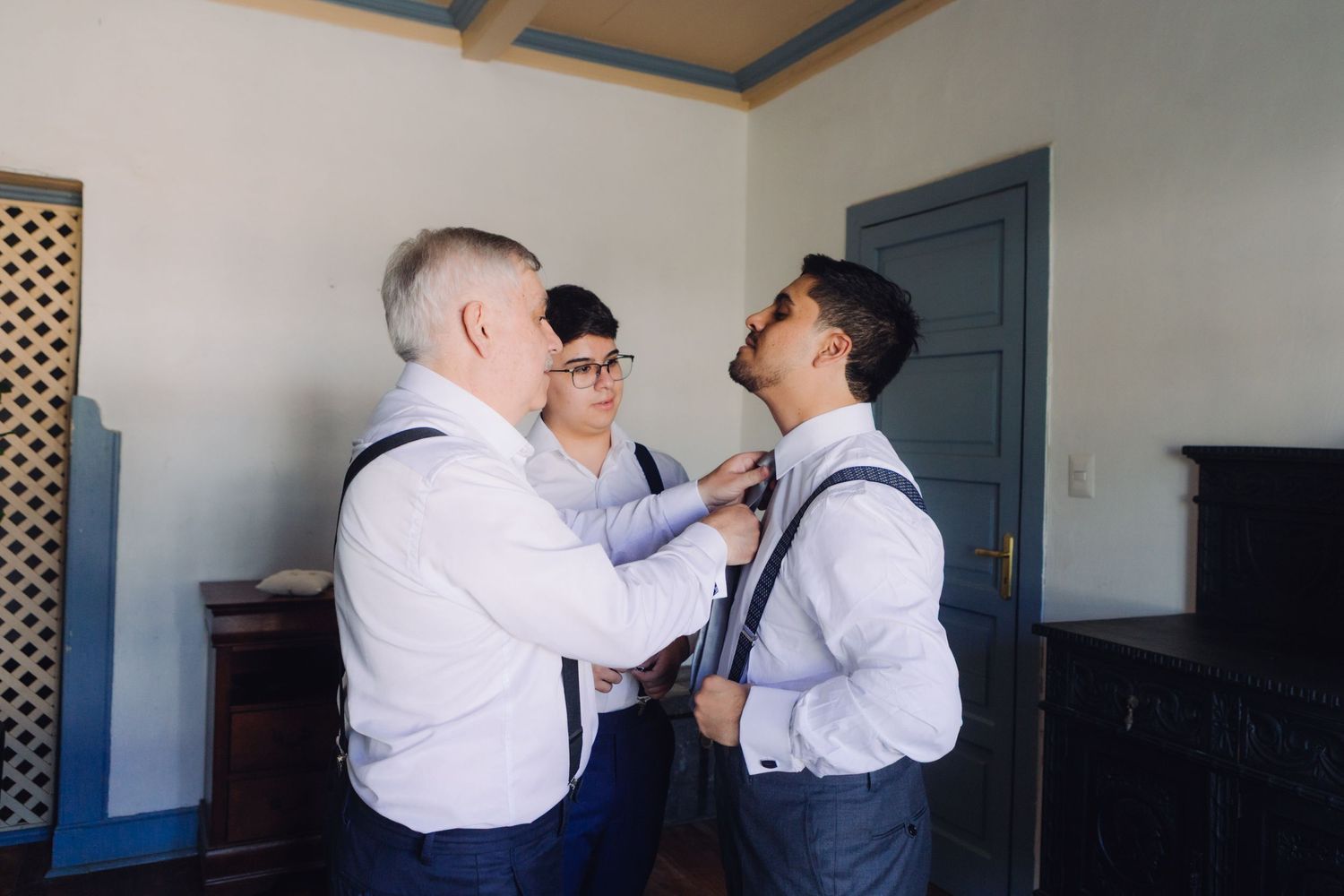 Groom being helped with tie by two groomsmen while getting ready for wedding.