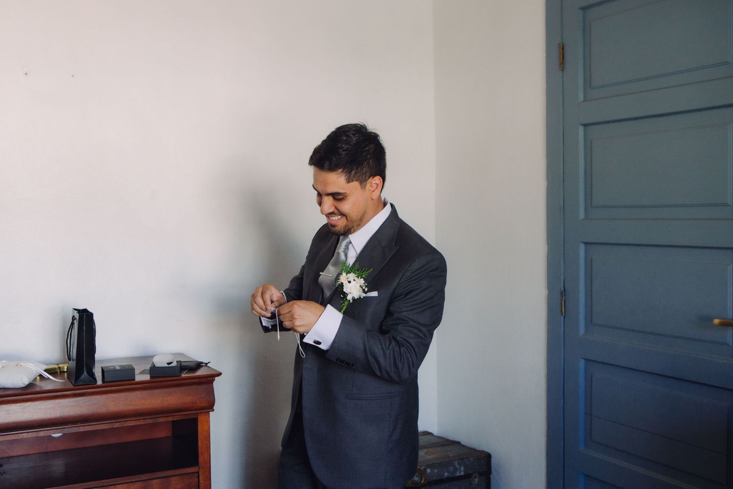 Groom in dark suit with boutonniere adjusting cufflinks before wedding ceremony.