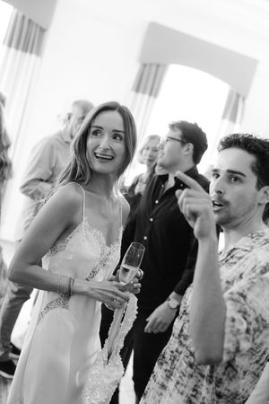 Black and white photo of a woman in a slip dress holding champagne, laughing with a man at a social gathering.