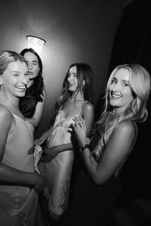 Four women laughing and dancing together at a party in black and white photo.