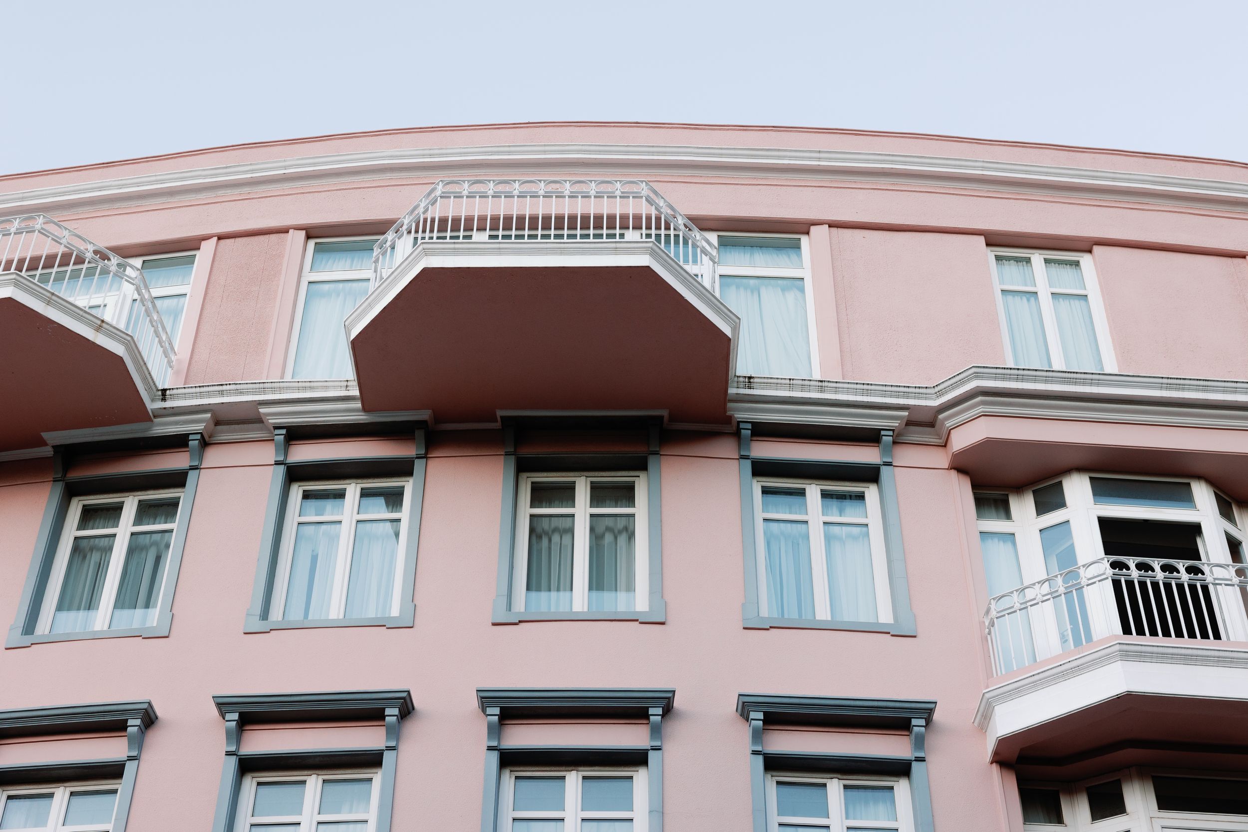 Pink curved apartment building facade with balconies and large windows against a clear sky.
