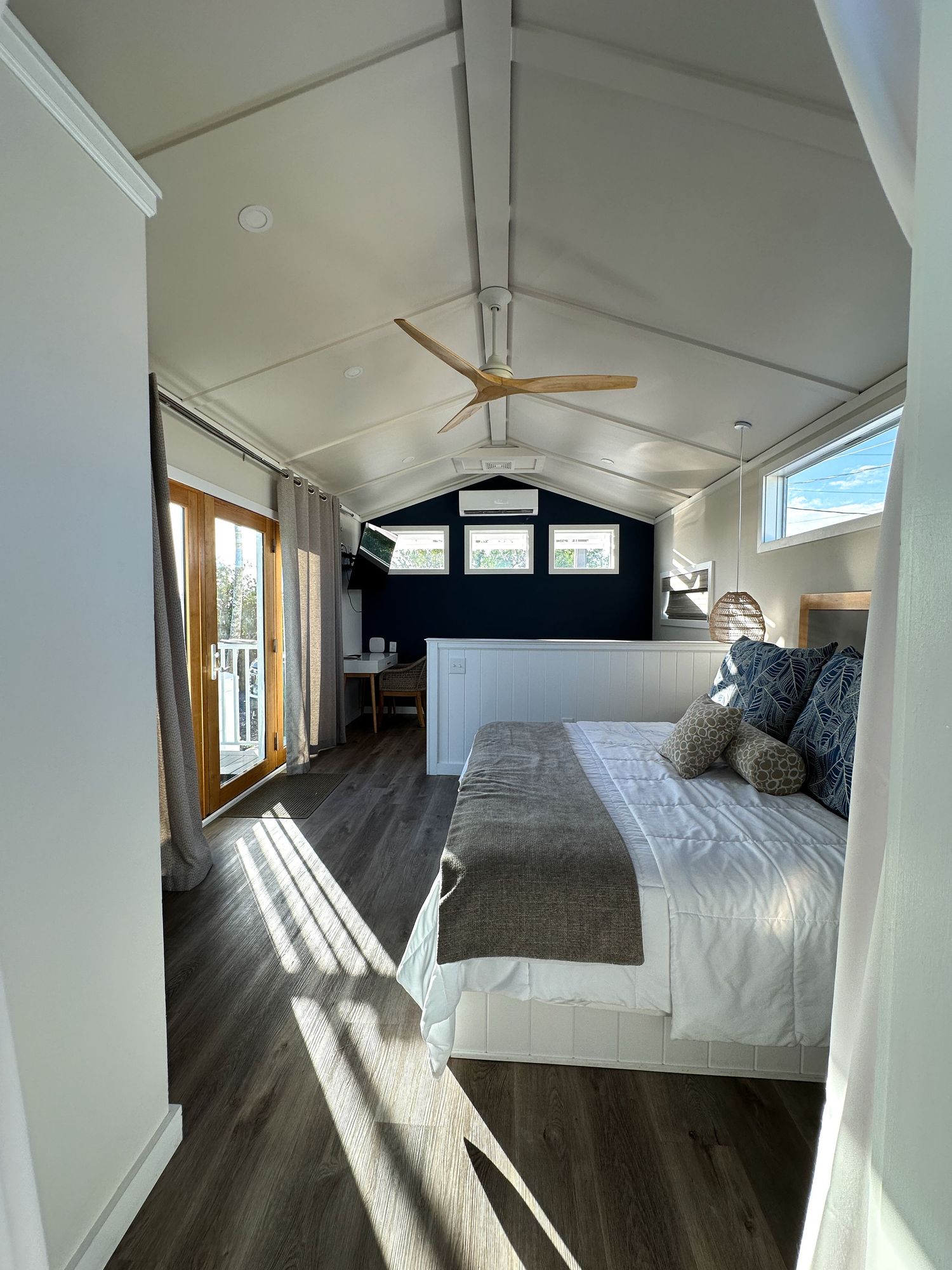 Bright tiny home bedroom with vaulted ceiling, ceiling fan, king bed, and French doors.