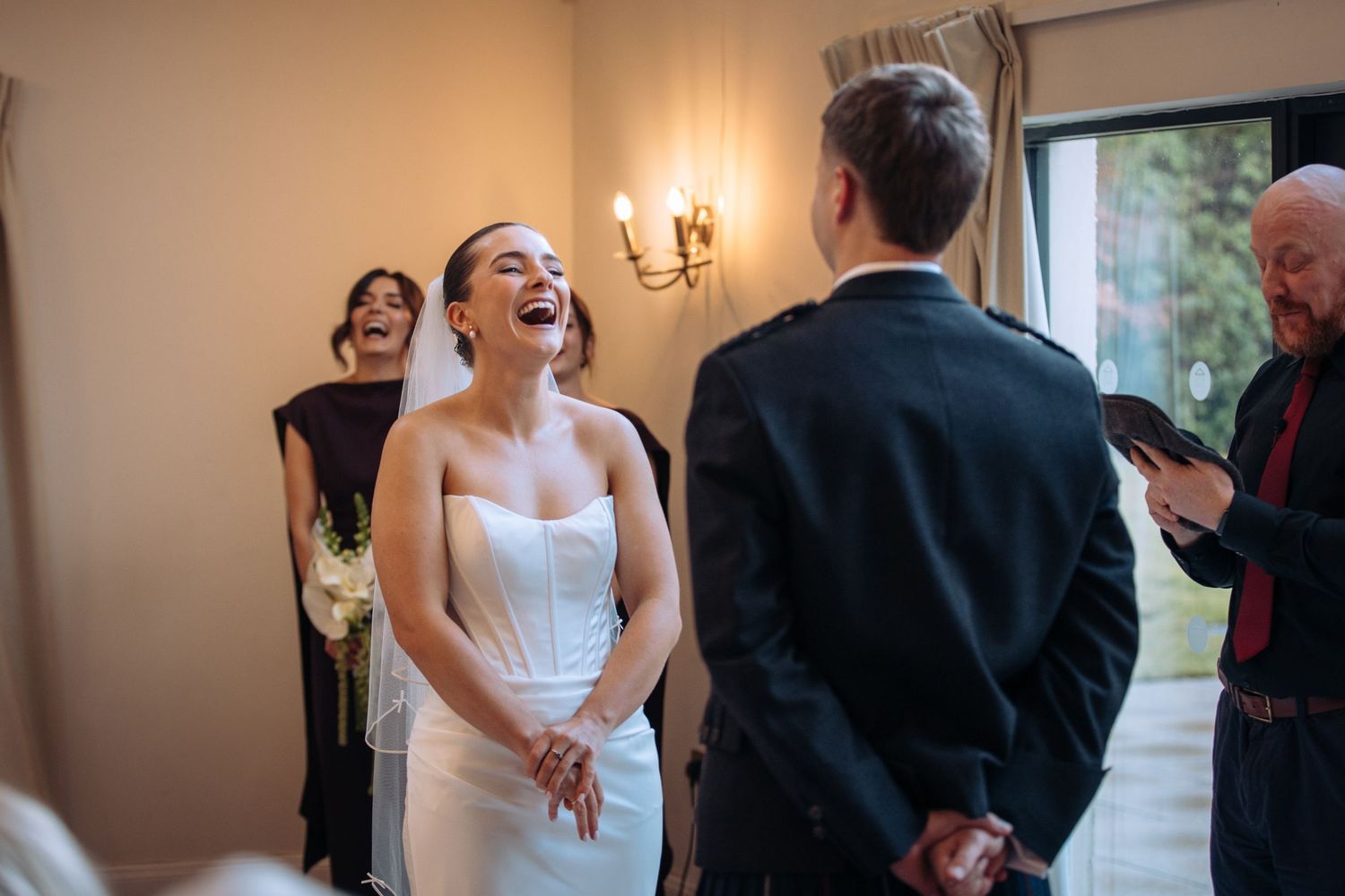 Bride laughing joyfully during wedding ceremony in elegant white strapless gown, sharing a happy moment with groom.
