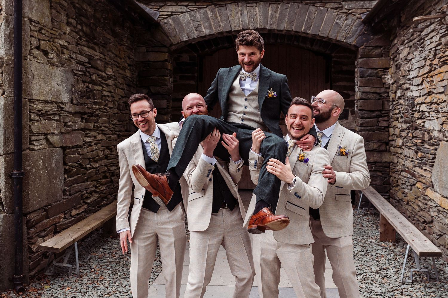 Wedding party poses outdoors with mountain views, bridesmaids in colorful gowns and groomsmen in navy tuxedos flanking the bride and groom.
