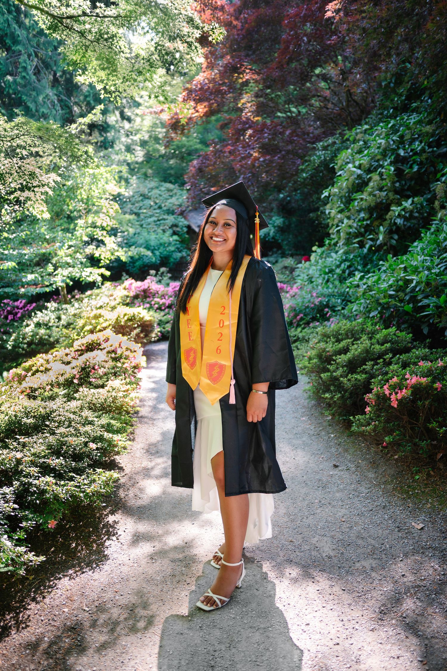 Graduate walking through the Yao Garden in her cap, gown and gold graduation stole