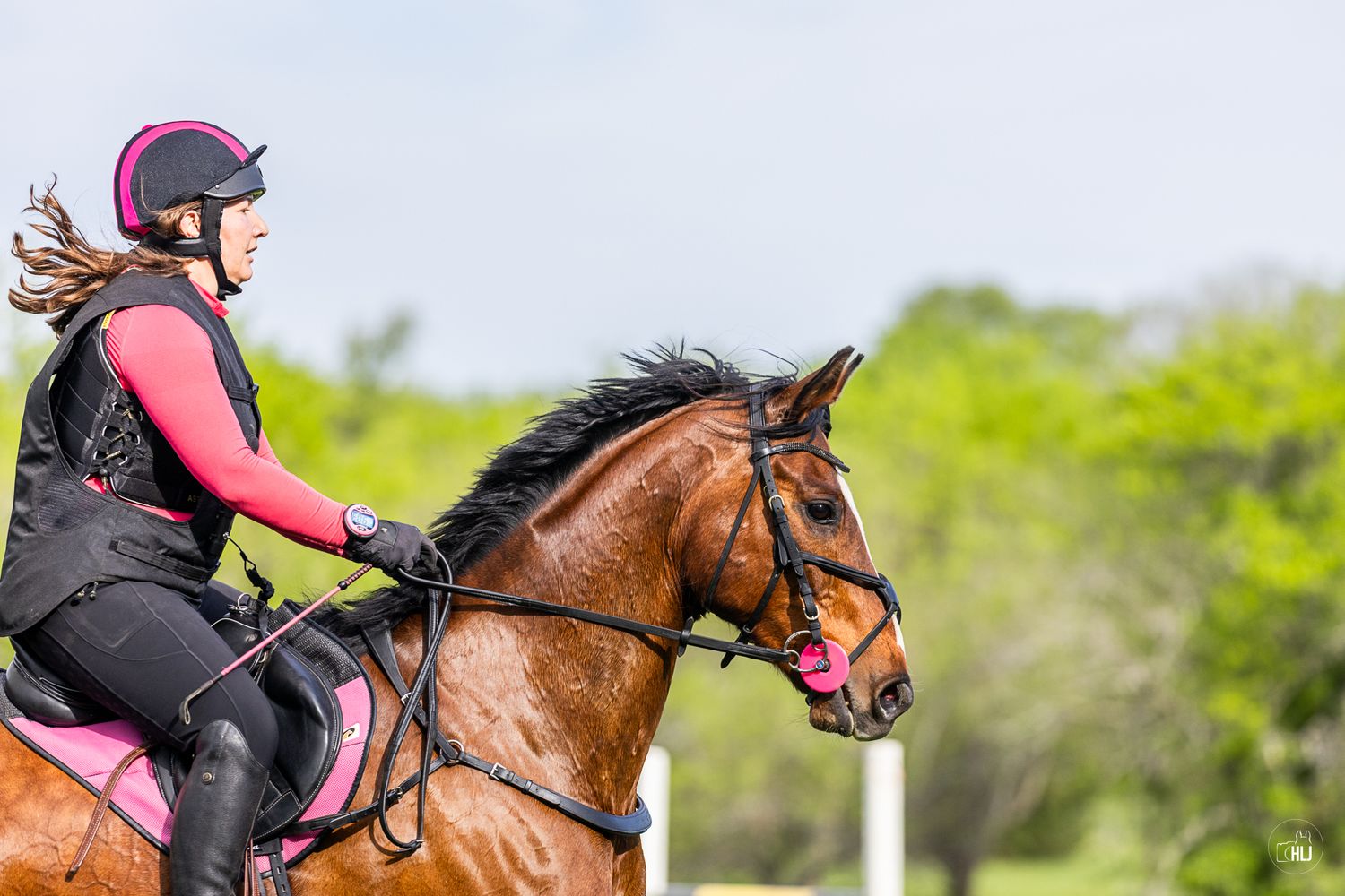 A rider in helmet jumps a gray horse over a white rail fence on a lush green grass field.
