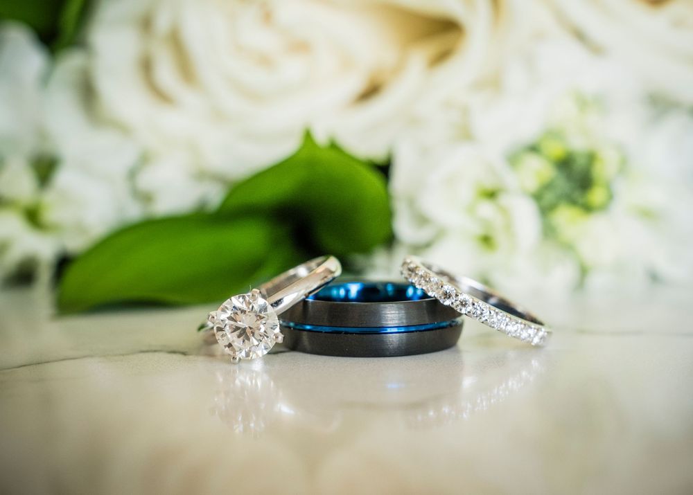 Three wedding rings including a blue tungsten band and two diamond rings displayed near white roses.