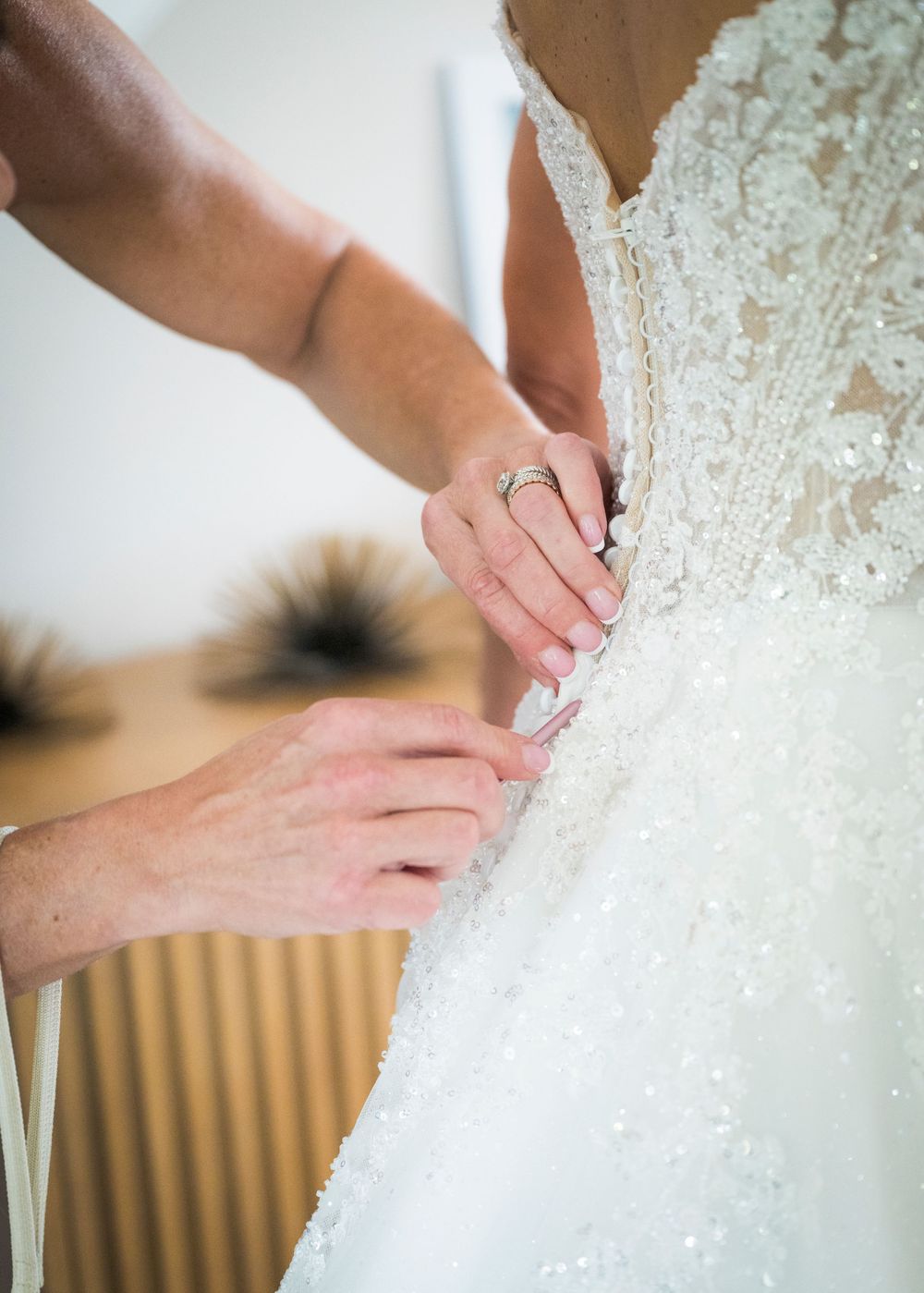 Hands fastening buttons on a beaded white wedding gown.