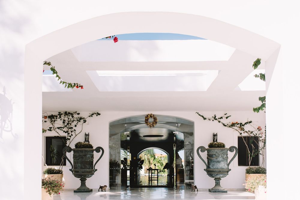 Elegant white arched entrance with ornate stone urns and wreath decor at a luxury Mediterranean-style villa.