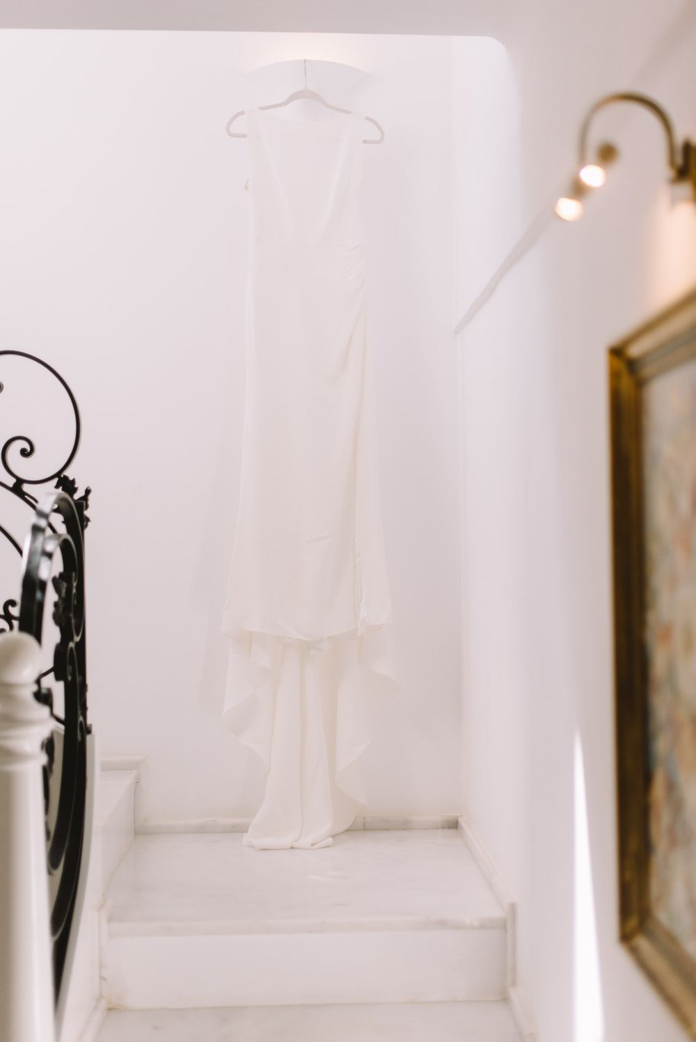 White wedding dress hanging on a hanger over white staircase in elegant venue with wrought iron railing.