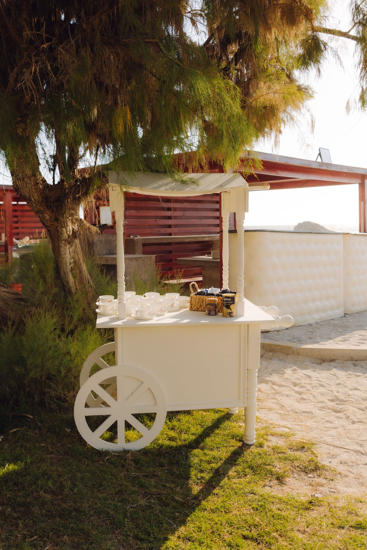 Charming white vintage cart decorated for a beach wedding under a shady tree.