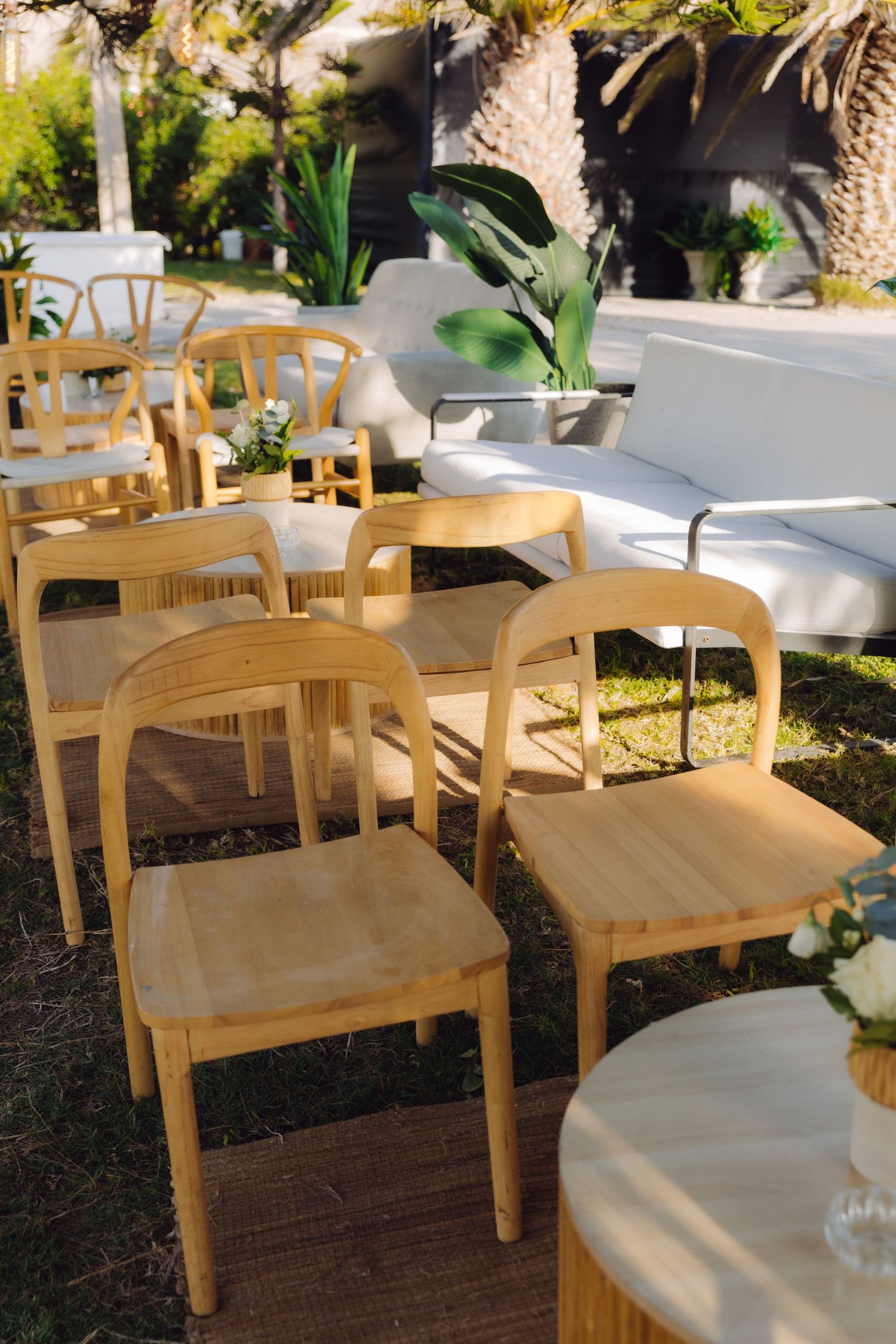 Natural wooden chairs arranged on deck at sunny outdoor wedding ceremony venue with white sofas.