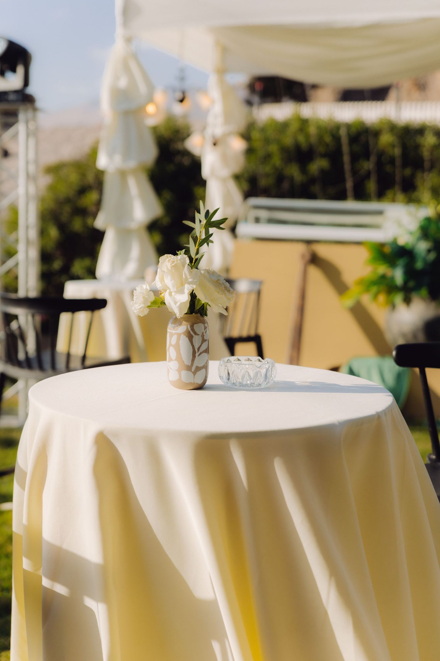 White linen cocktail table with floral arrangement and ashtray at outdoor wedding reception venue.