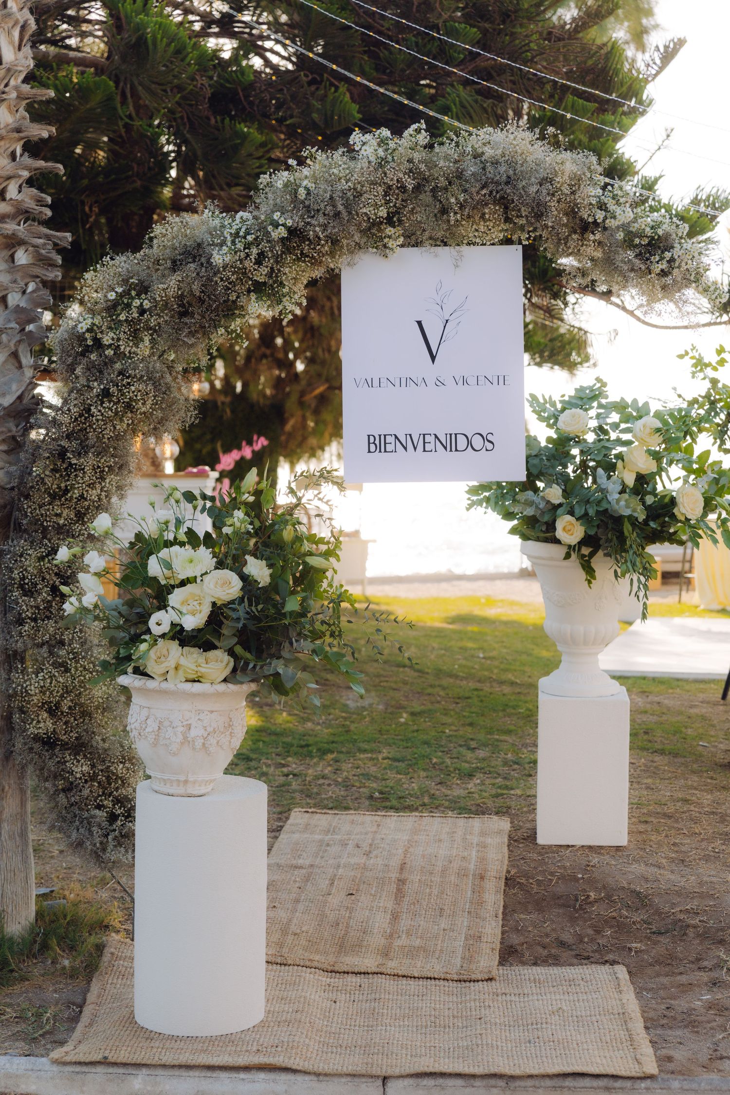 Wedding welcome arch decorated with white flowers and greenery displaying Valentina and Vicente sign.