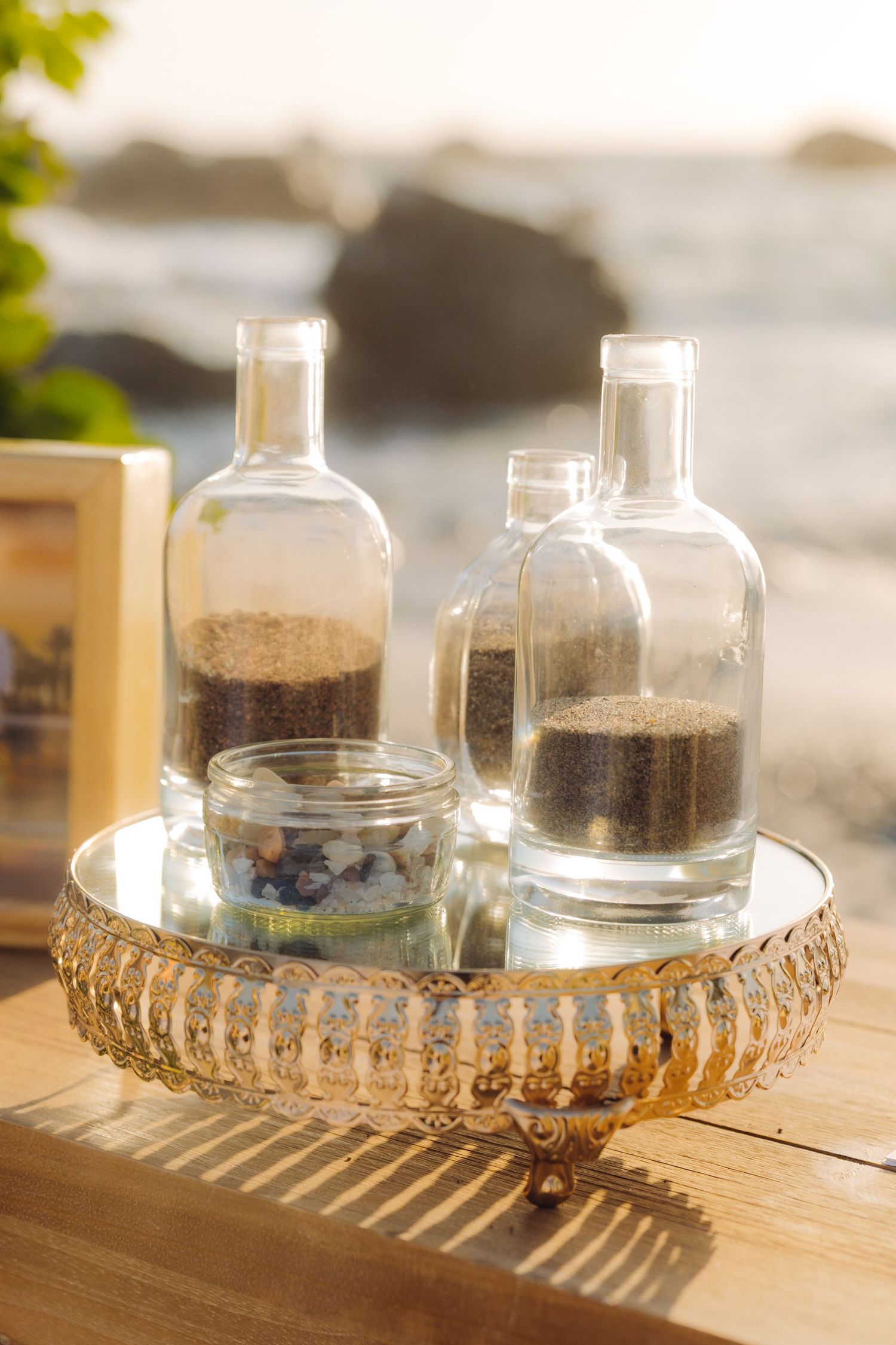 Glass bottles with layered sand on gold mirrored tray for beach wedding unity ceremony display.