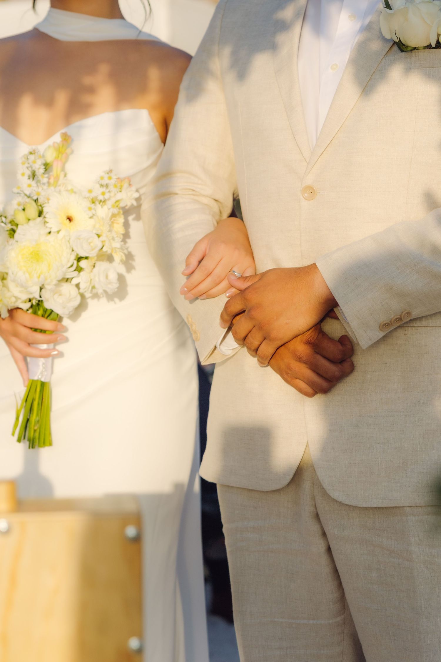 Close-up of bride and groom holding hands at wedding ceremony with white floral bouquet.