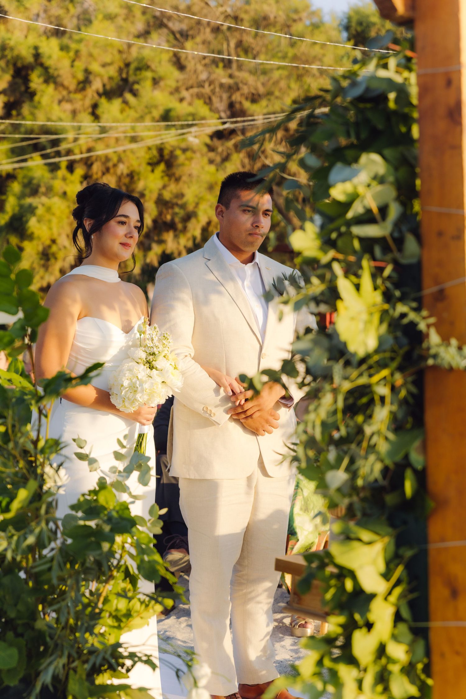 Bride and groom standing at a vine-covered wedding altar during an outdoor ceremony.
