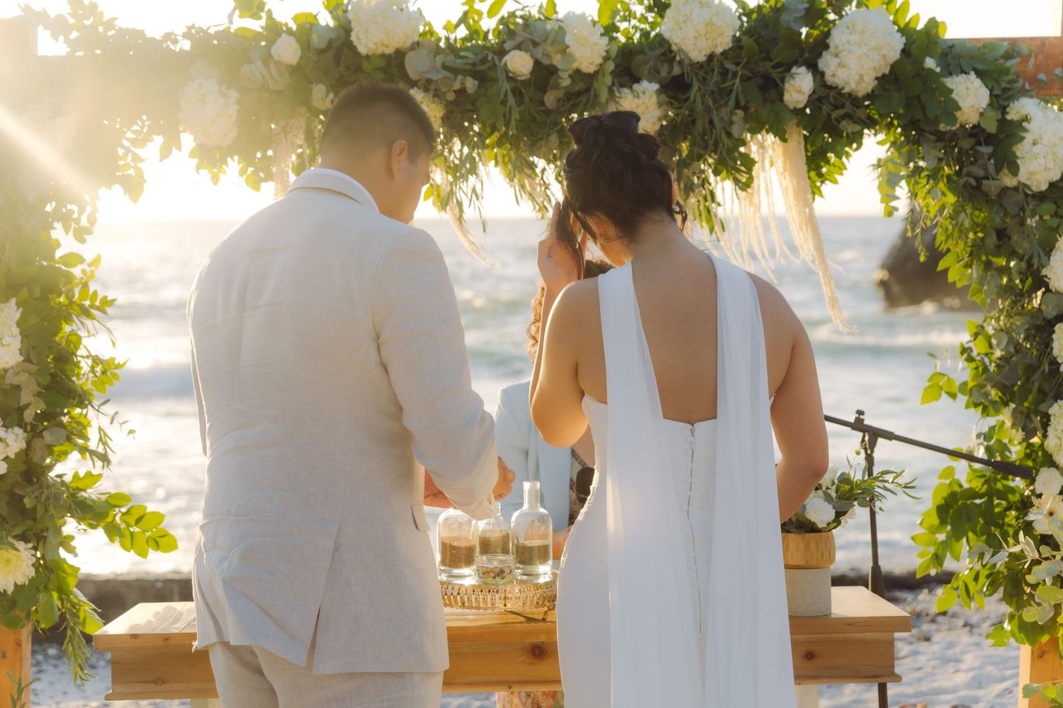 Couple standing at a floral arch altar on the beach at sunset during their wedding.
