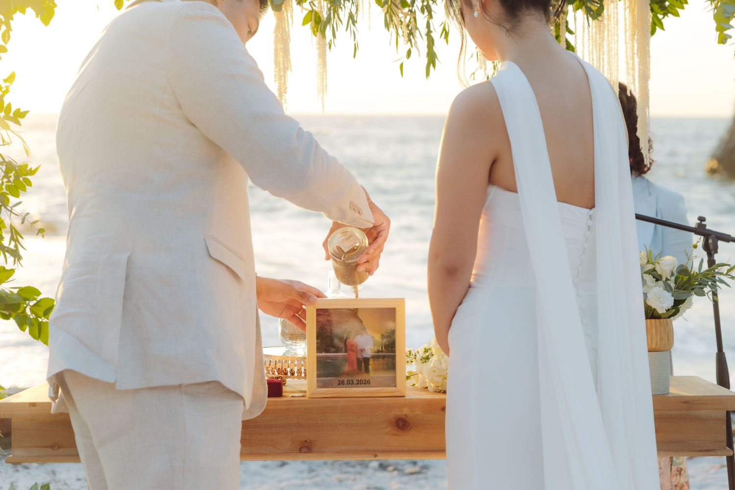 Couple performs unity sand ceremony at beach wedding at golden sunset by the ocean.