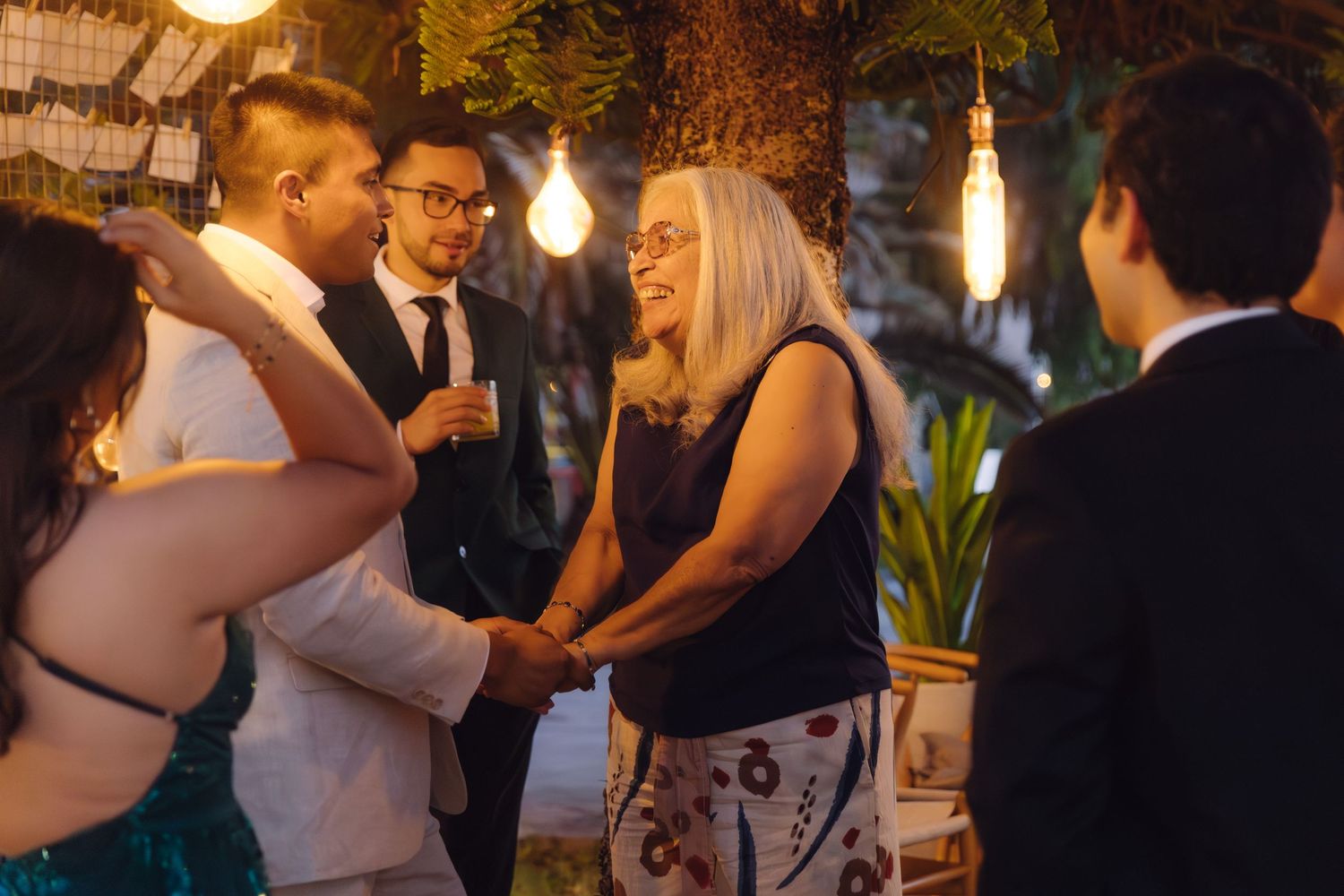 Wedding guests share a joyful moment with the bride and groom at an outdoor evening reception.
