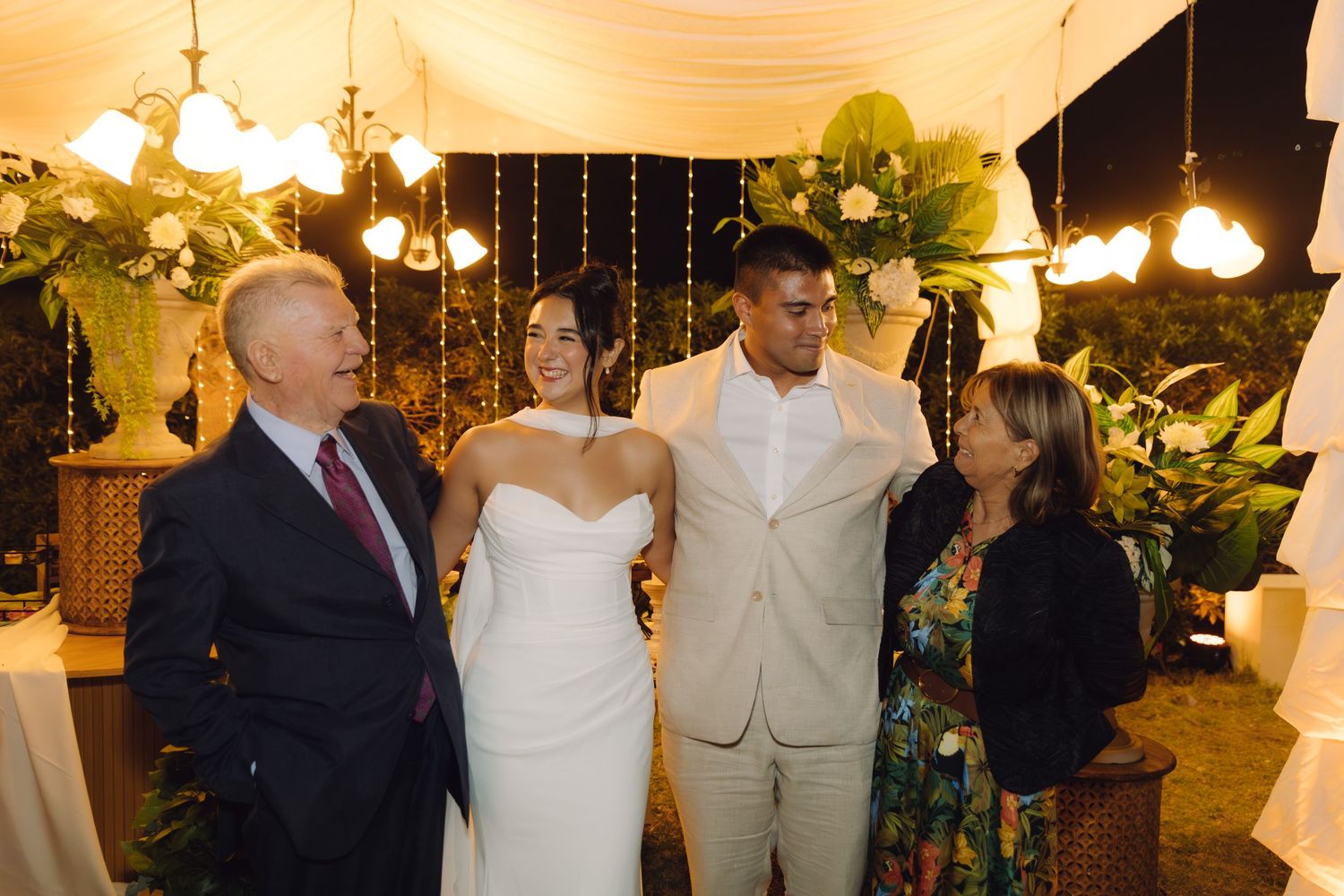 Happy newlyweds pose with family members at a beautifully decorated outdoor wedding reception.