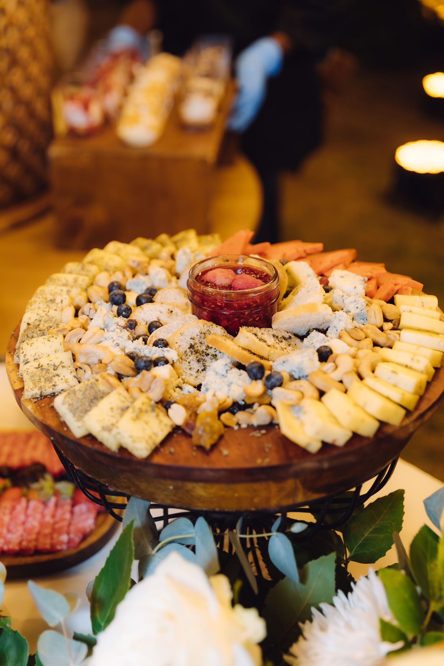 Round wooden charcuterie board with cheese, blueberries, crackers, and jam at wedding.