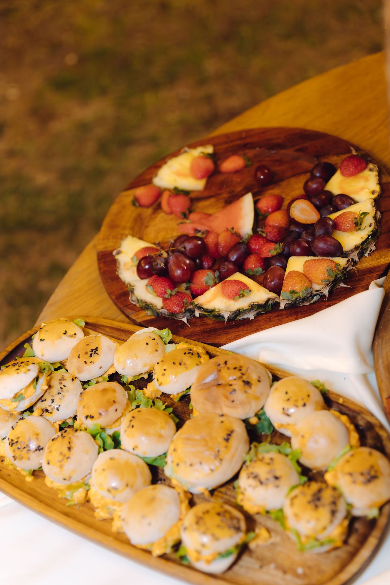 Wedding appetizer display with mini sliders and fresh fruit on wooden serving boards.
